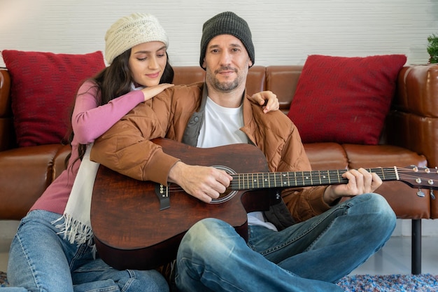 Pareja romántica sentada en el suelo. Hombre tocando la guitarra con una mujer disfrutando de un gran momento juntos en casa