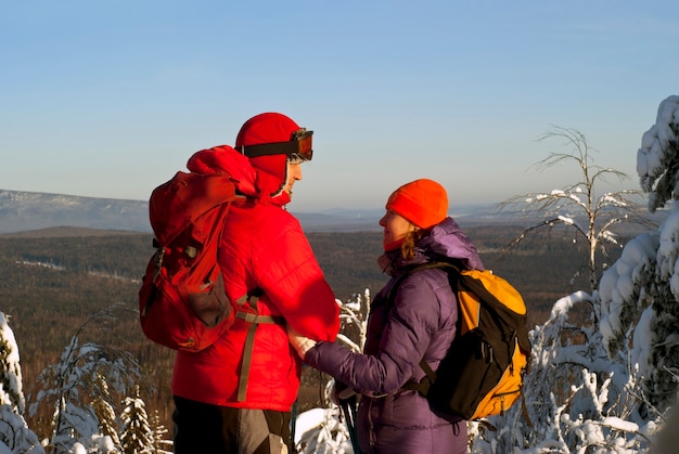 Pareja en ropa de invierno con mochilas miran de pie en la cima de la montaña