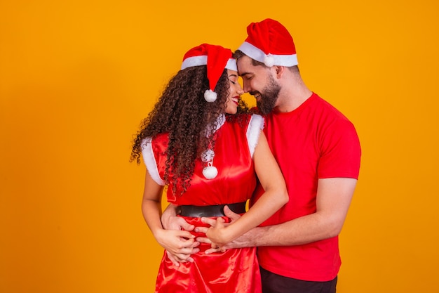 Pareja de San Valentín sonriente en traje de Navidad abrazados aislados en retrato de estudio de fondo amarillo. Feliz año nuevo celebración concepto de vacaciones.