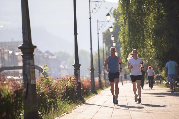 pareja sana y madura trotando en la ciudad a primera hora de la mañana con el amanecer en el fondo