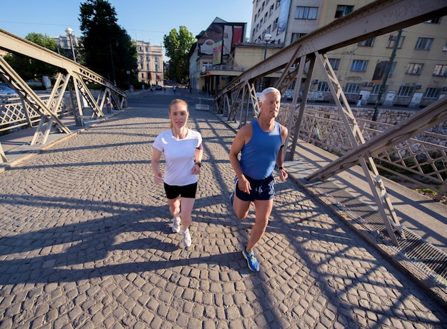 pareja sana y madura trotando en la ciudad a primera hora de la mañana con el amanecer en el fondo