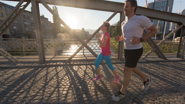 pareja sana y madura trotando en la ciudad a primera hora de la mañana con el amanecer en el fondo