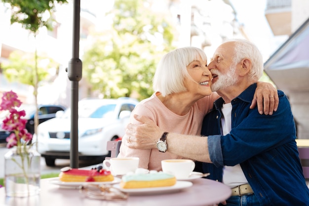 Pareja senior alegre coqueteando y sentado en el café