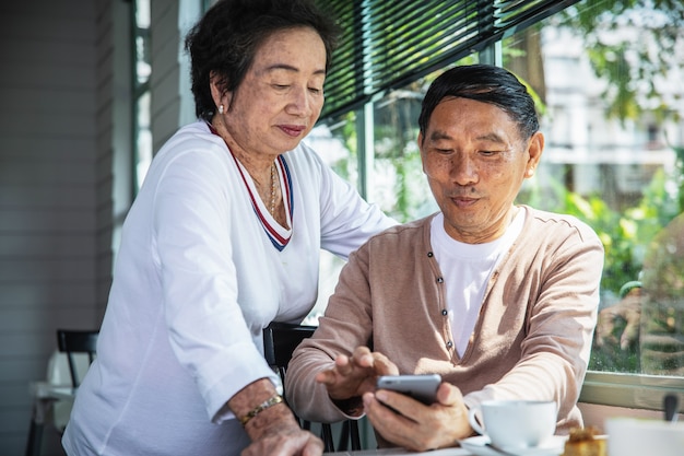 Pareja senior asiática mirando smartphone mientras teatime