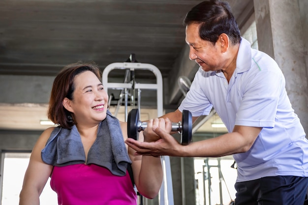 Pareja senior asiática sonriendo en ropa deportiva haciendo ejercicio en el gimnasio.