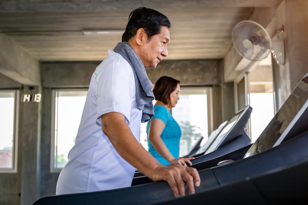 Pareja senior asiática sonriendo en ropa deportiva haciendo ejercicio en el gimnasio.