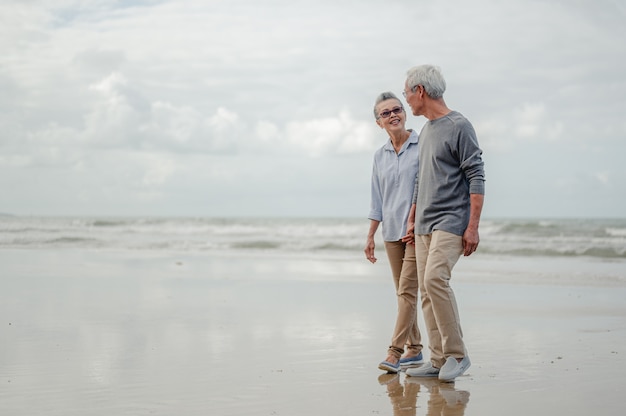 Pareja senior cogidos de la mano y caminar por la playa, planificar un seguro de vida en el concepto de jubilación.