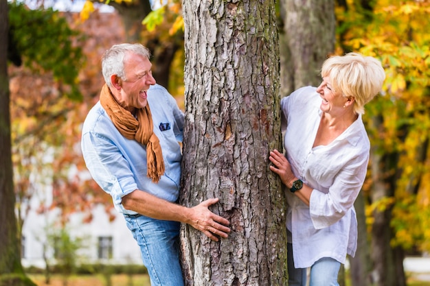 Pareja Senior coqueteando jugando alrededor del árbol en el parque