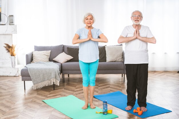 Pareja senior deportiva haciendo ejercicios de fitness y relajación en casa - Ancianos entrenando para mantenerse sanos y en forma