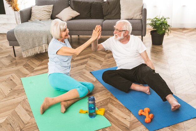 Pareja senior deportiva haciendo ejercicios de fitness y relajación en casa - Ancianos entrenando para mantenerse sanos y en forma