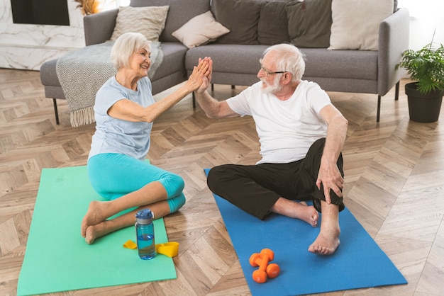 Pareja senior deportiva haciendo ejercicios de fitness y relajación en casa - Ancianos entrenando para mantenerse sanos y en forma