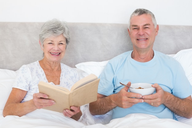 Pareja Senior con libro y tazón de fuente en la cama