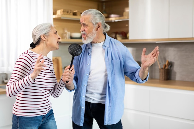 Pareja senior positiva divirtiéndose en el interior de la cocina cantando y bailando