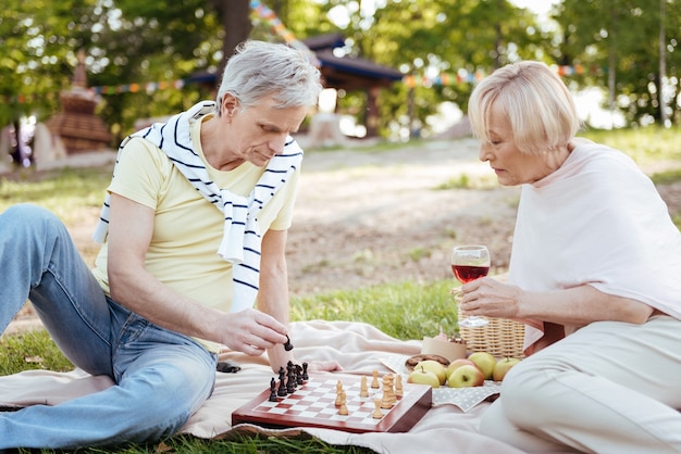 Pareja senior positiva inteligente que expresa tranquilidad mientras juega al ajedrez y descansa al aire libre