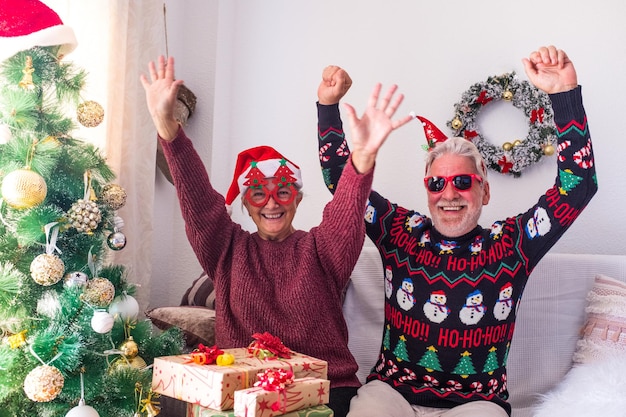 Pareja senior en ropa de abrigo y gorro de Papá Noel bailando y celebrando frente al árbol de Navidad decorado en casa. Amantes de la vieja pareja heterosexual romántica celebrando juntos el festival de navidad