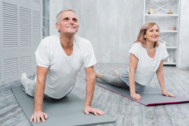 Pareja senior sonriente realizando ejercicios de estiramiento en casa