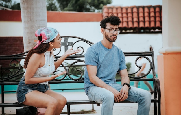 Pareja sentada en un banco del parque discutiendo Una pareja joven discutiendo sentado en un parque Concepto de parejas agresivas en el parque Pareja molesta discutiendo en un banco del parque