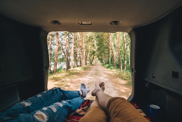 Una pareja sentada en el maletero de un SUV disfrutando de la vista de la naturaleza en un coche de senderismo