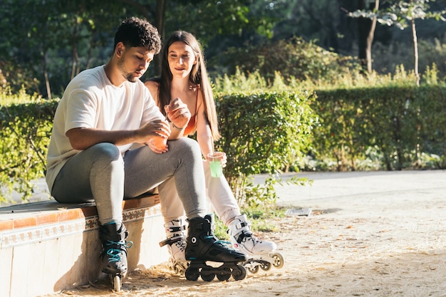 Pareja sentada en un parque bebiendo refrescos con patines en línea