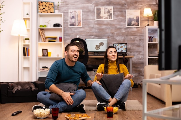 Pareja sentada en el suelo y viendo la televisión en su sala de estar.