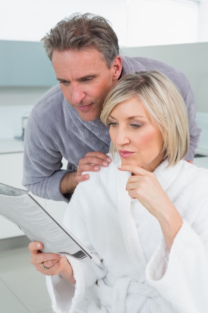 Pareja seria en albornoces leyendo periódico