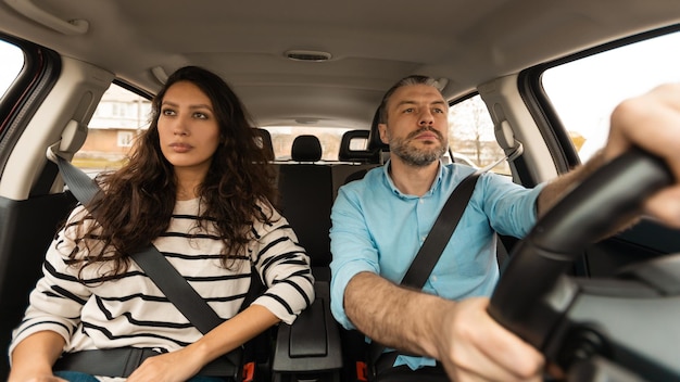 Una pareja seria conduciendo sentada en un automóvil disfrutando del panorama del viaje