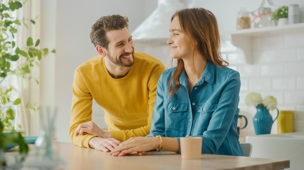 Una pareja se sienta en una mesa en su casa, sonriendo y mirándose.