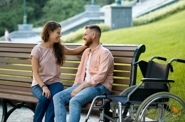 Pareja con silla de ruedas relajándose en un banco en el parque