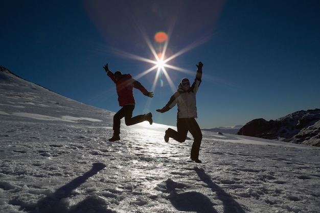 Pareja de silueta saltando sobre la nieve contra el sol y el cielo azul