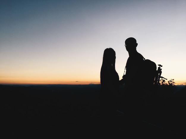 Pareja de siluetas en el paisaje contra el cielo durante la puesta de sol