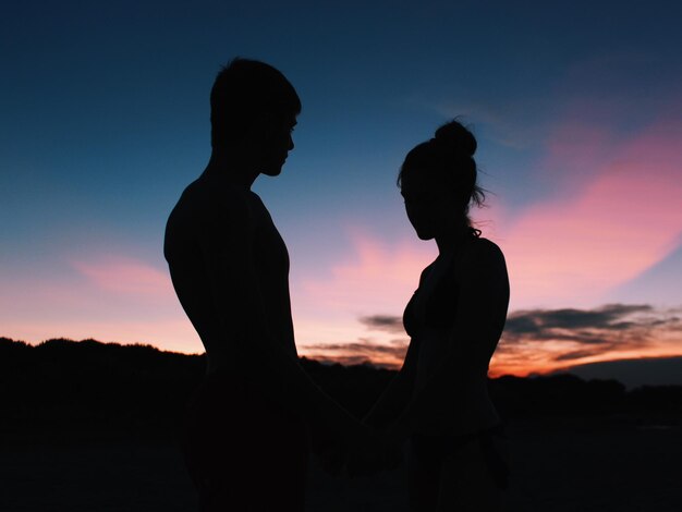 Una pareja de siluetas de pie contra el cielo durante la puesta de sol