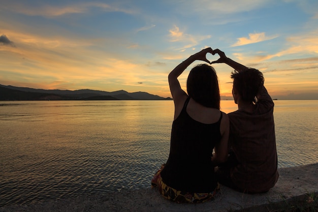 Pareja con el símbolo del dedo del corazón al atardecer