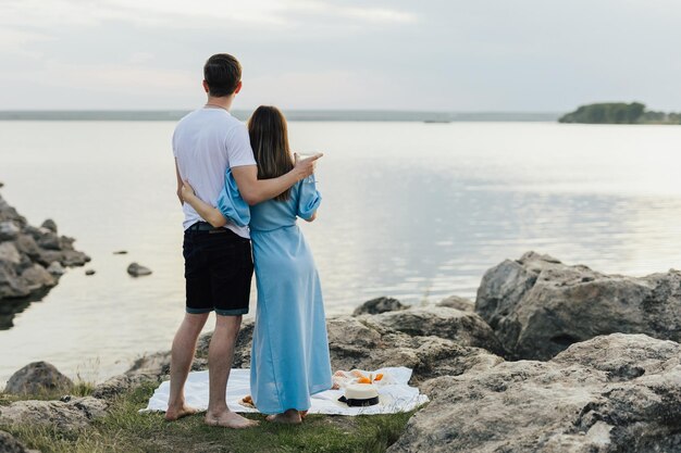 Una pareja se para sobre una manta junto al agua, mirando el agua.