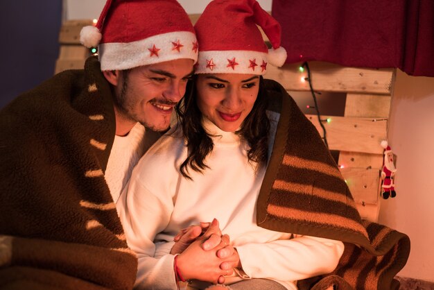 Pareja con sombreros de navidad tomados de la mano en una noche de invierno frente a la cálida luz de la estufa