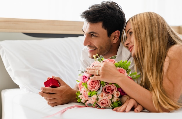 Pareja sonriendo feliz con amante en la cama mientras sostiene casarse caja de anillo en las manos