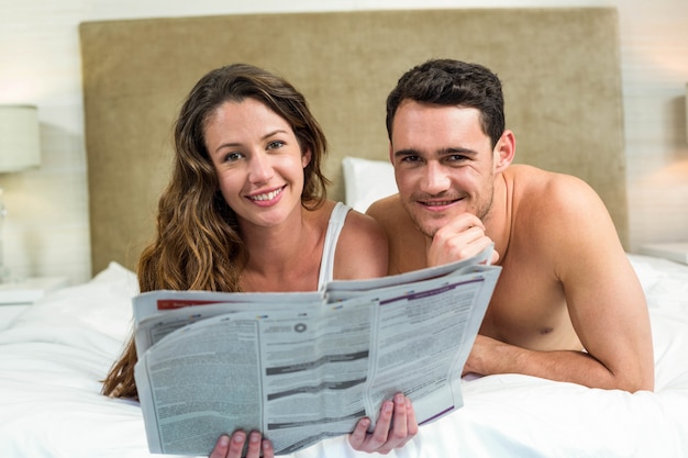 Pareja sonriente acostado en la cama con un periódico