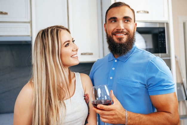 Pareja sonriente alegre cocinar y beber vino en la cocina de casa