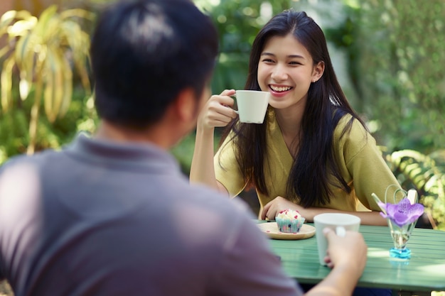 Pareja sonriente asiática disfrutando de fecha hablando y tomando café en el café al aire libre