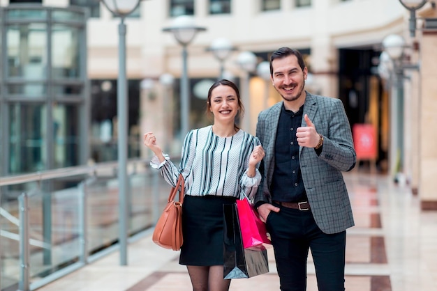 Una pareja sonriente de aspecto moderno en un centro comercial están haciendo un gesto de aprobación y están felices