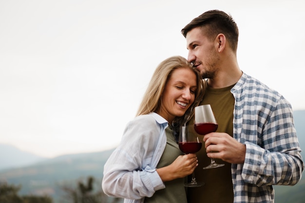 Pareja sonriente brindando copas de vino al aire libre en las montañas, retrato de cerca