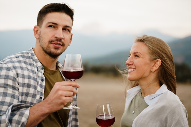 Pareja sonriente brindando copas de vino al aire libre en las montañas