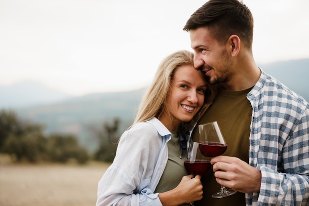 Pareja sonriente brindando copas de vino al aire libre en las montañas