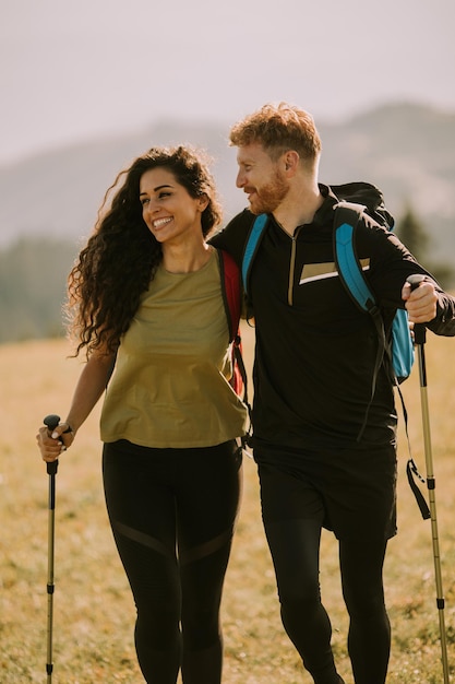 Pareja sonriente caminando con mochilas sobre colinas verdes