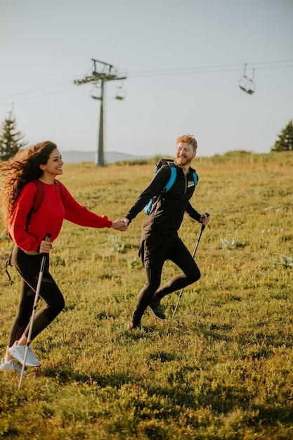 Pareja sonriente caminando con mochilas sobre verdes colinas junto al telesilla