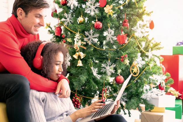 La pareja sonriente está sentada en el sofá comprando en línea con la computadora portátil en la acogedora habitación.