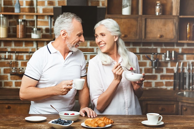 Pareja sonriente mirándose desayunando en la cocina