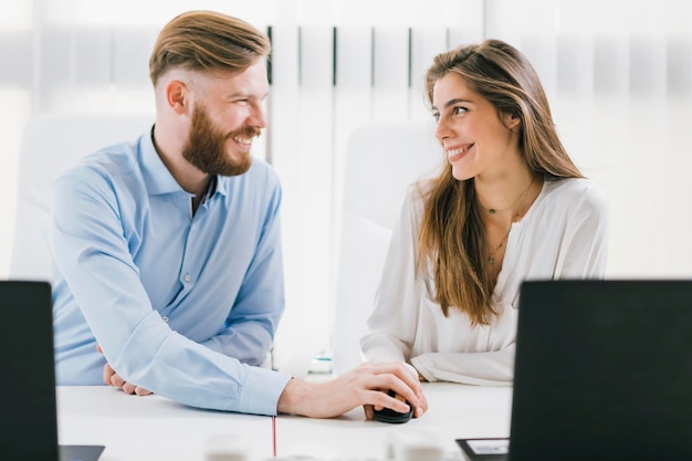 Una pareja sonriente mirándose mientras trabajan en la oficina