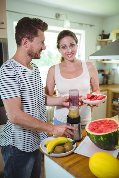 Pareja sonriente preparando batido de frutas en la cocina