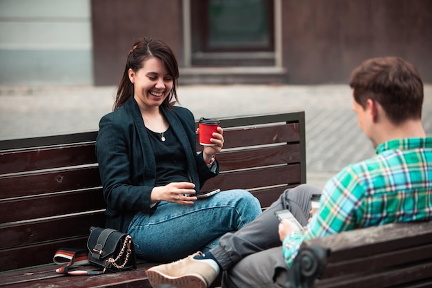 Pareja sonriente sentada en un banco hablando entre ellos bebiendo café