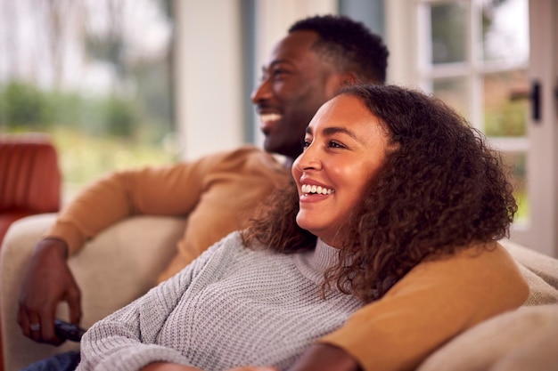 Pareja sonriente sentada en el sofá en casa viendo la televisión juntos